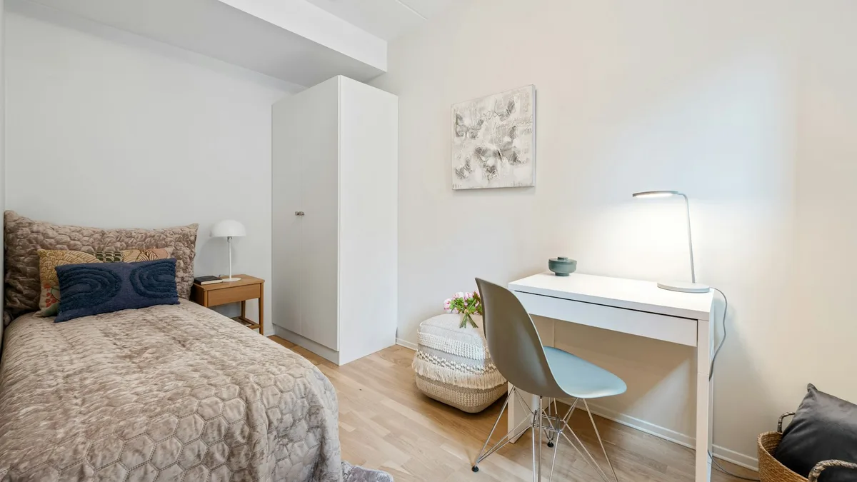 Chambre lumineuse avec un lit simple, un bureau blanc et une armoire